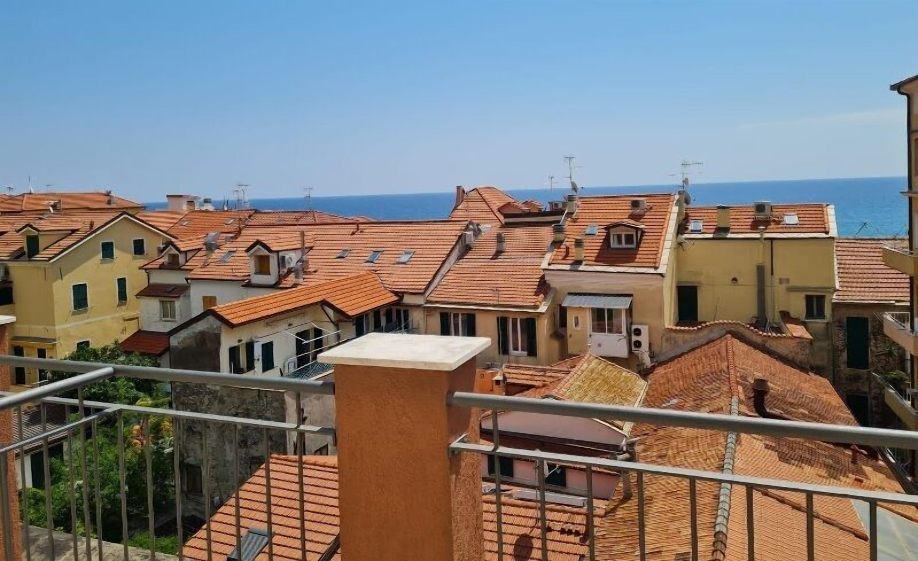 A coastal residential area with terracotta-roofed buildings, some with visible balconies and air conditioning units.