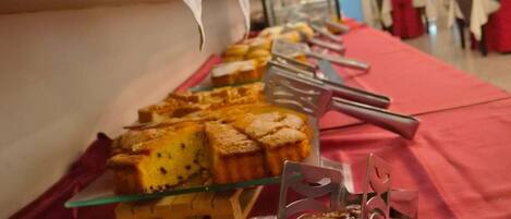 A buffet table with various dishes, including a cake and a meat dish, in a room with red chairs and a blue wall.