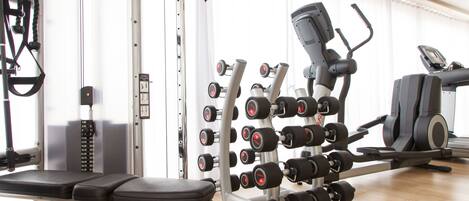 Uma academia com diversos equipamentos de exercício, incluindo halteres, um banco e aparelhos de cardio.