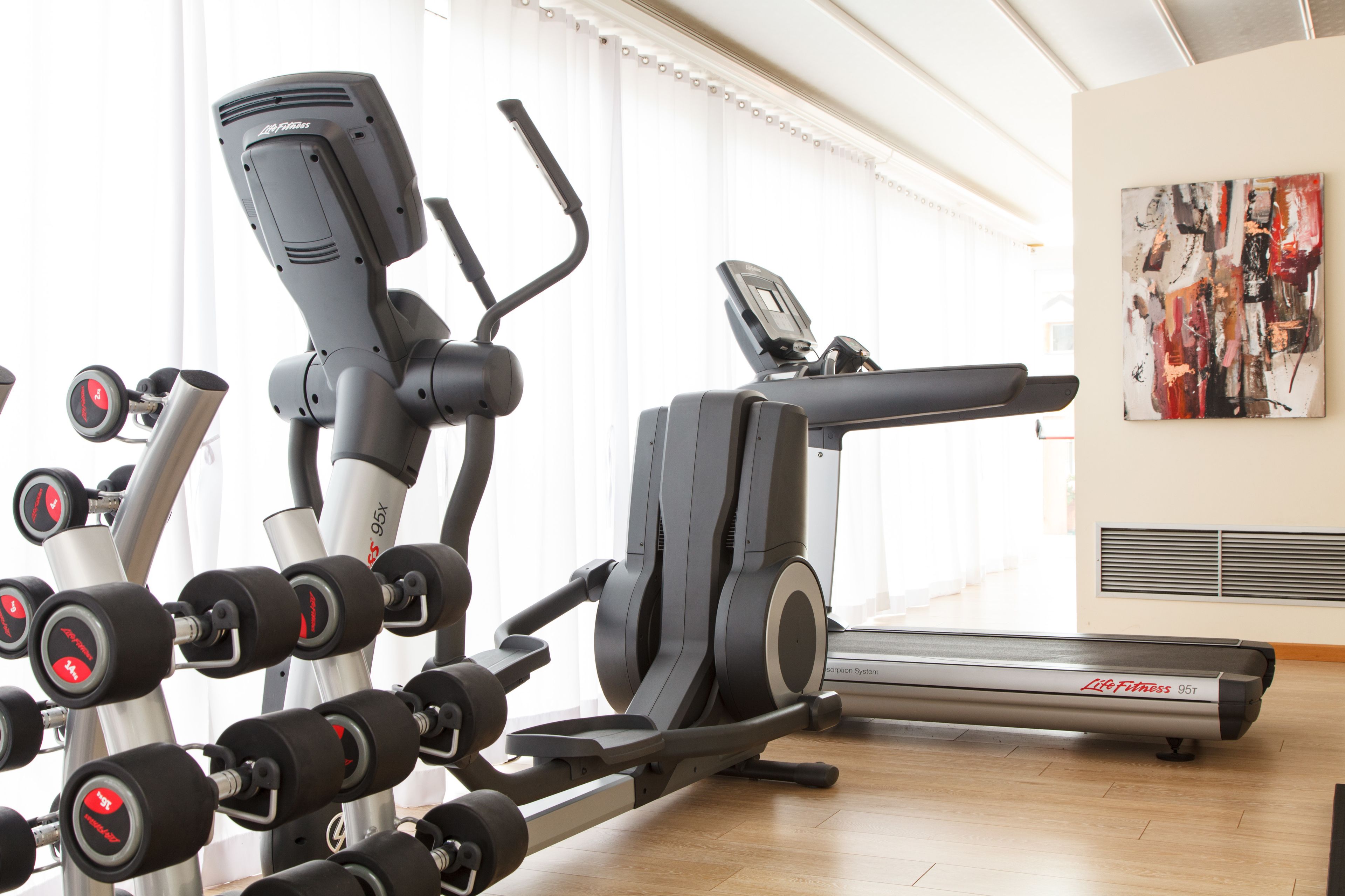 A gym with cardio machines, dumbbells, and a treadmill.