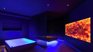 Una habitación moderna con una cama, una camilla de masaje fijada a la pared y una pared grande iluminada.