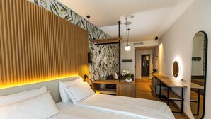Una habitación de hotel moderna con una cama grande, un cabecero de madera, un escritorio con espejo y un pequeño rincón de descanso.