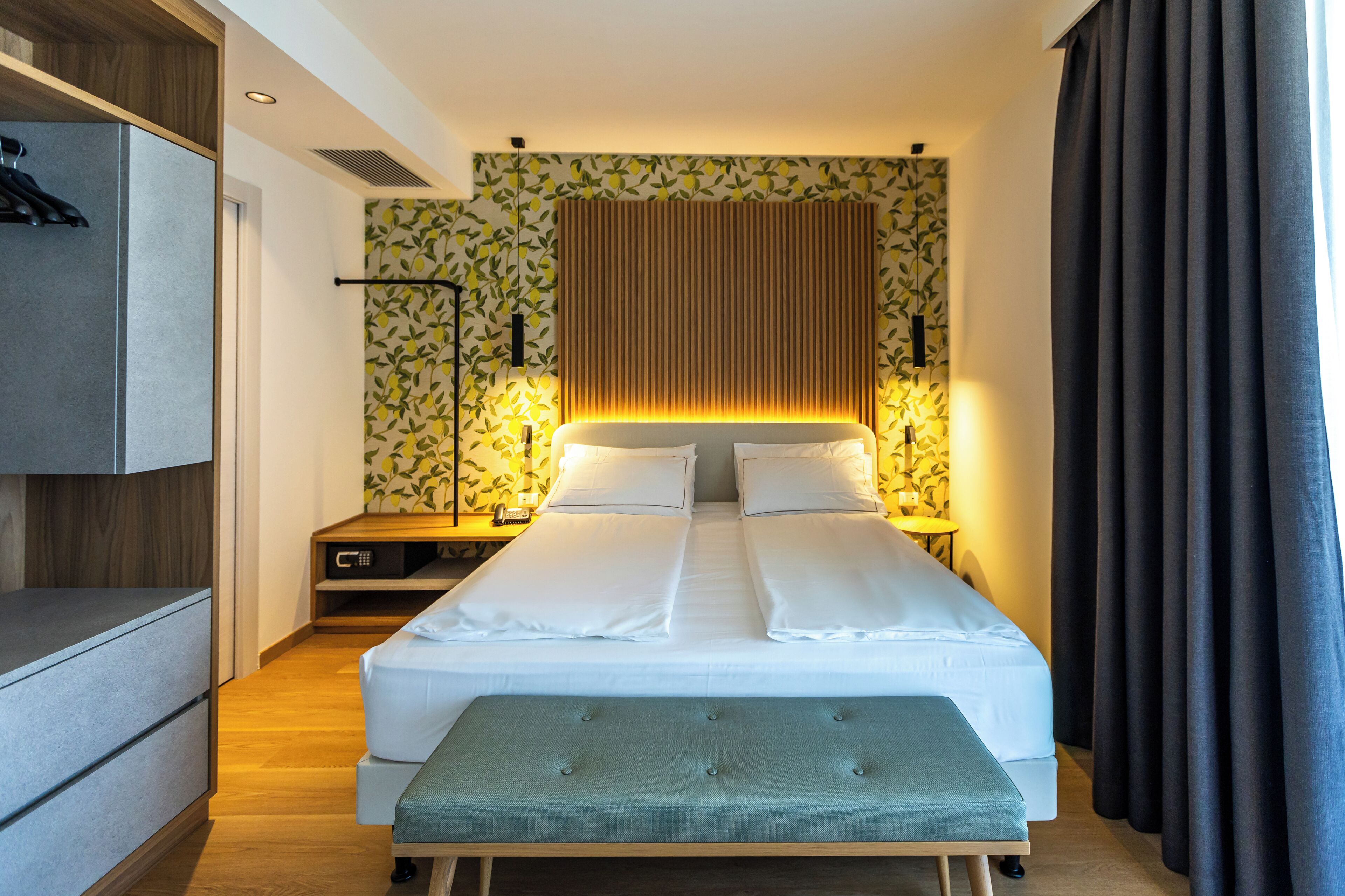 Camera d'albergo moderna con un letto ben rifatto, un comodino con una lampada, un armadio e una panca.