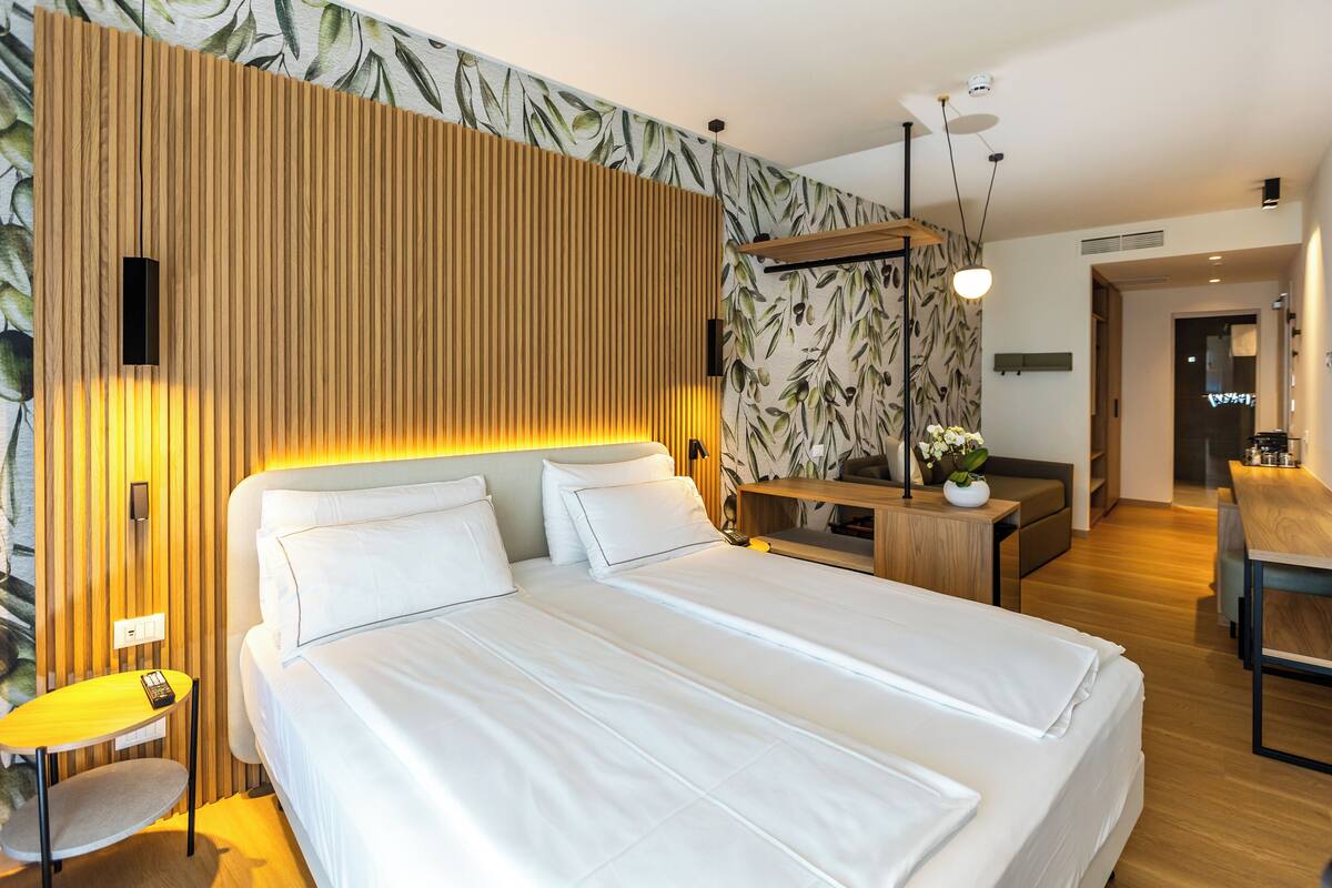 Une chambre d’hôtel moderne dotée d’un grand lit, d’un mur décoratif en bois, d’un bureau avec une chaise et d’un petit coin salon.