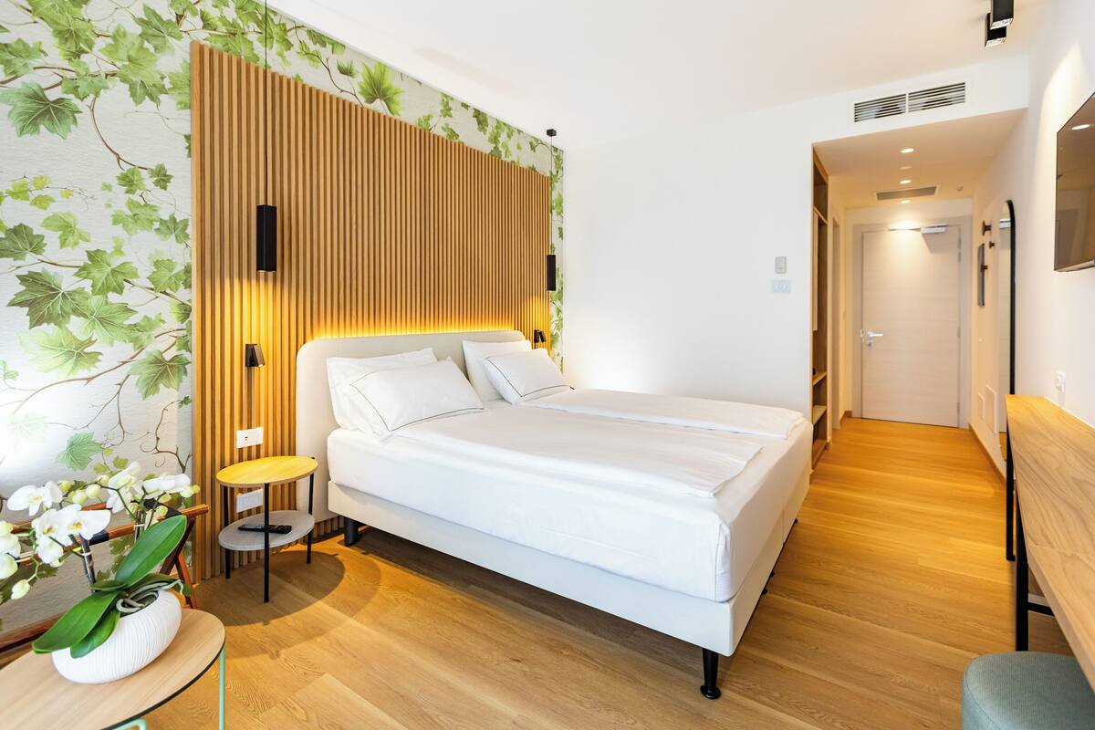 Une chambre d’hôtel moderne avec un grand lit, une petite table de chevet, un téléviseur fixé au mur et un décor mural en panneaux de bois.