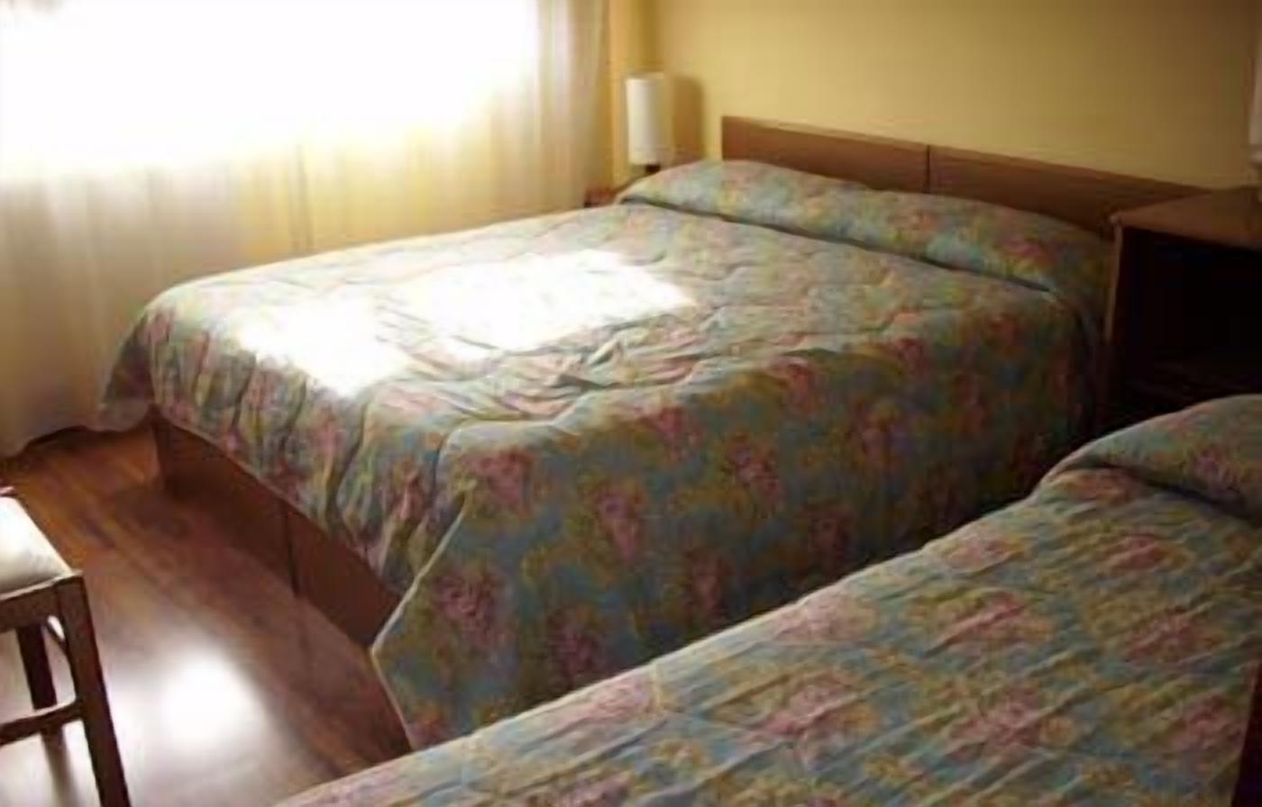 Een kamer met twee bedden, een houten vloer, een nachtkastje en een lamp.