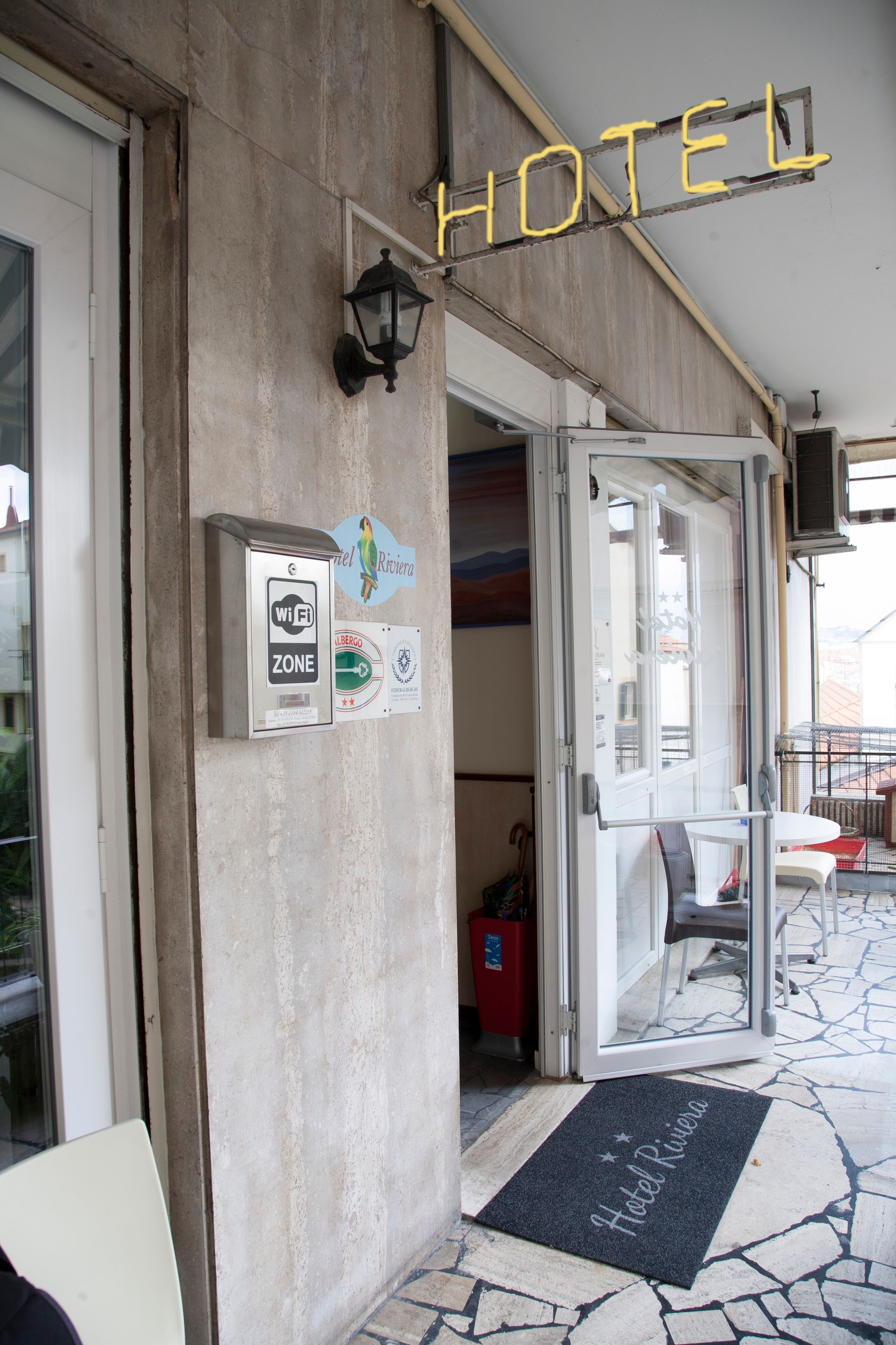Ein Hotel Eingang mit einem 'HOTEL'-Schild, einem Schild für die WLAN-Zone und einer Fußmatte mit dem Schriftzug 'Hotel Riviera'.