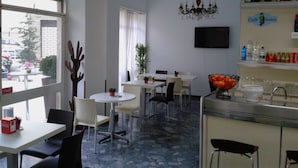 Un espace repas moderne avec des tables et des chaises rondes, un lustre et un bar doté d’étagères remplies de boissons.