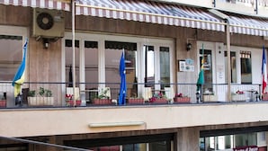 Un hôtel doté d’un balcon, de plantes en pot et de drapeaux.