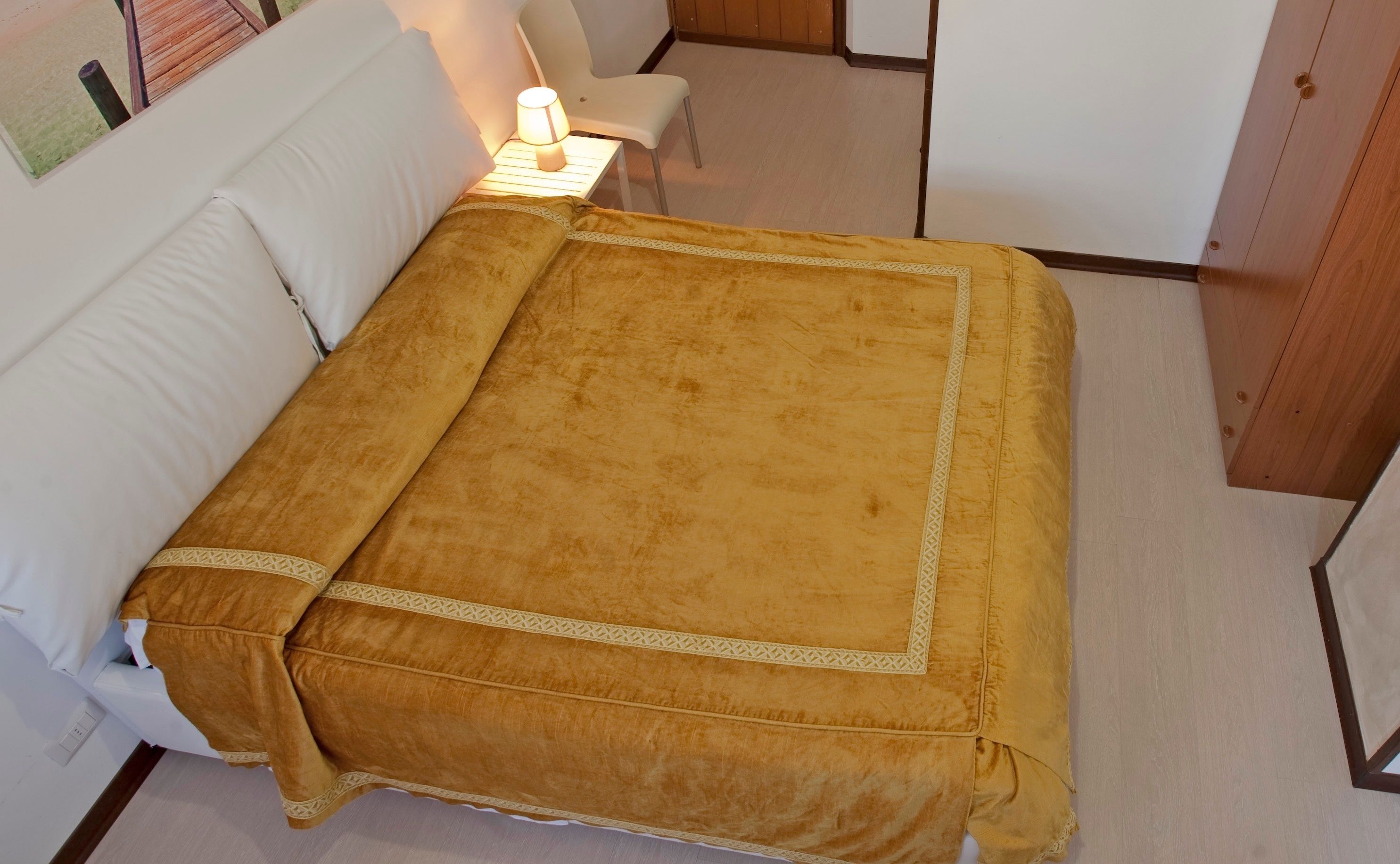 A bed with a yellow bedspread and white pillows in a room with a wooden floor and white walls.