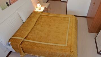 A bed with a yellow bedspread and white pillows in a room with a wooden floor and white walls.