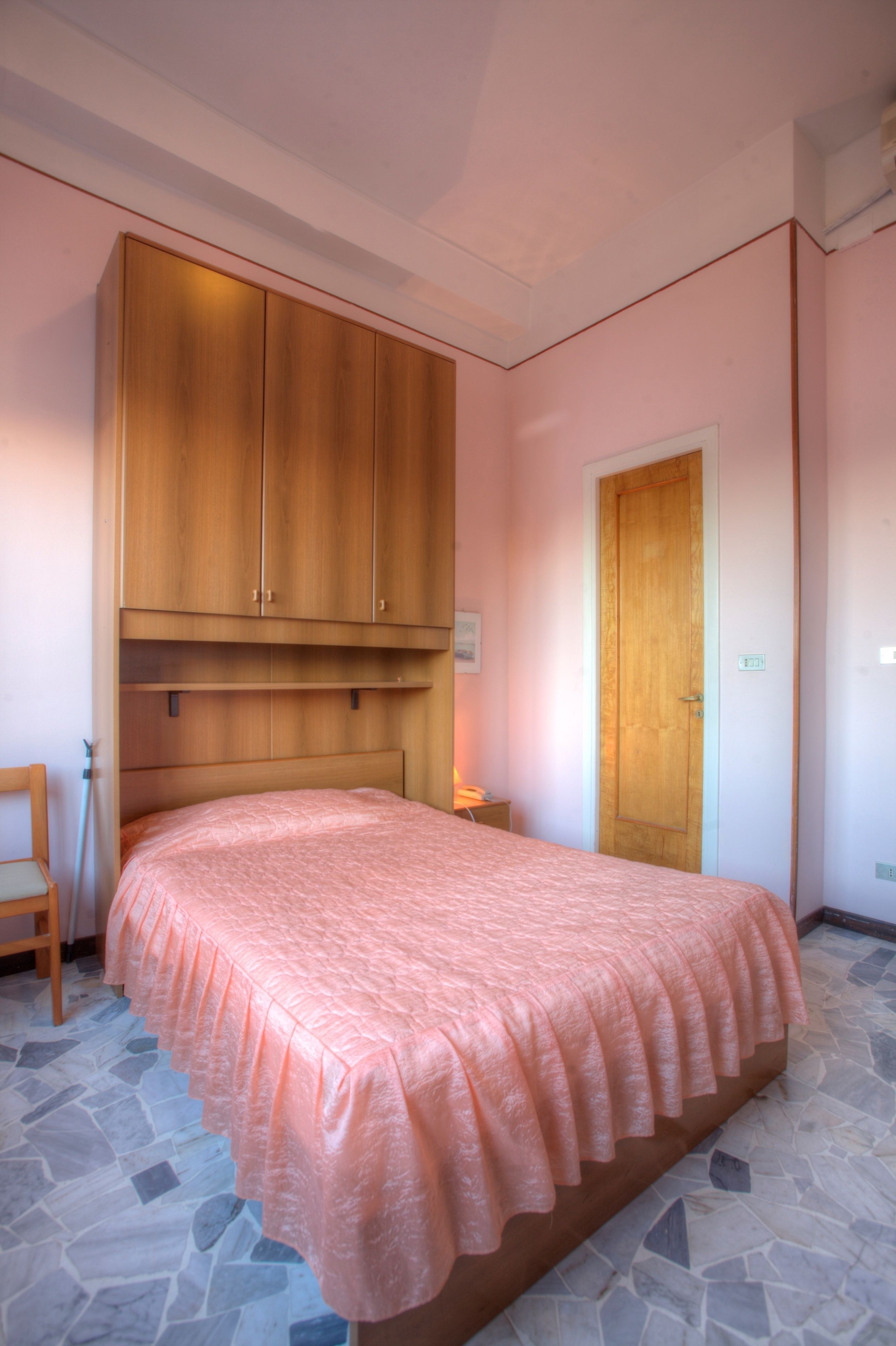 A bedroom with a bed, a wooden wardrobe, a door, and a chair.