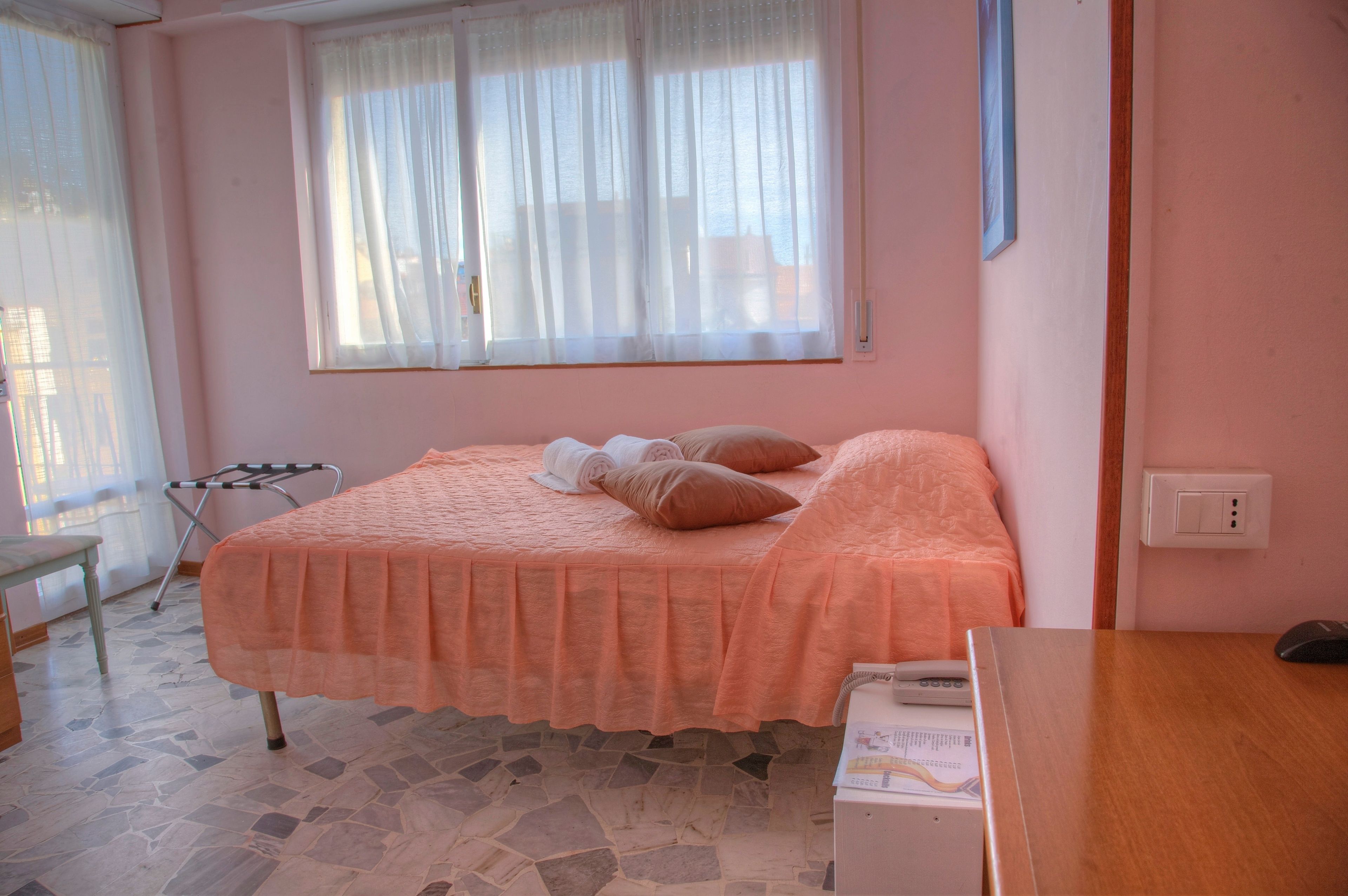 A bedroom with a bed, a chair, a table, and a window with curtains.