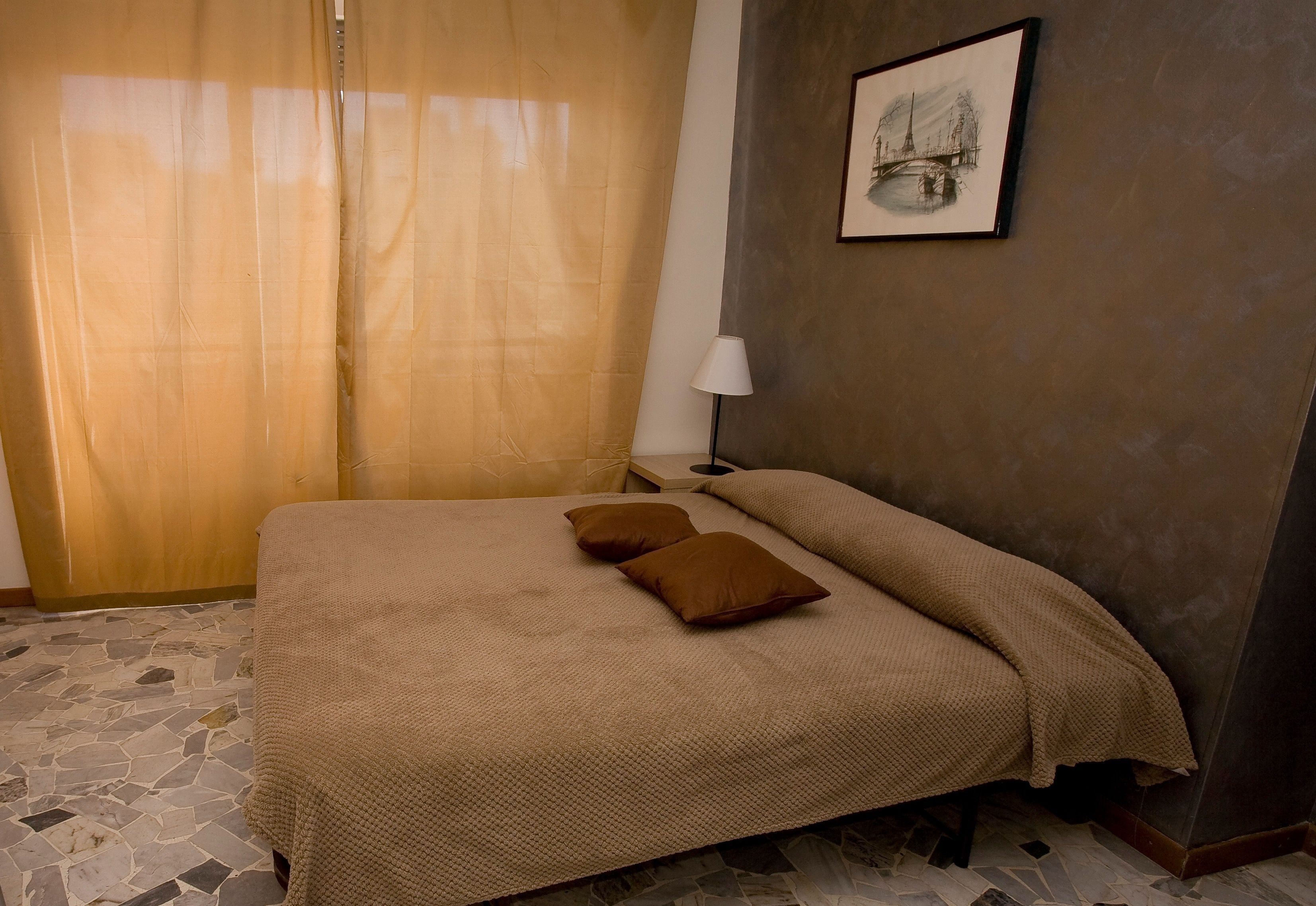 A bedroom with a bed, a nightstand, a lamp, and a painting on the wall.