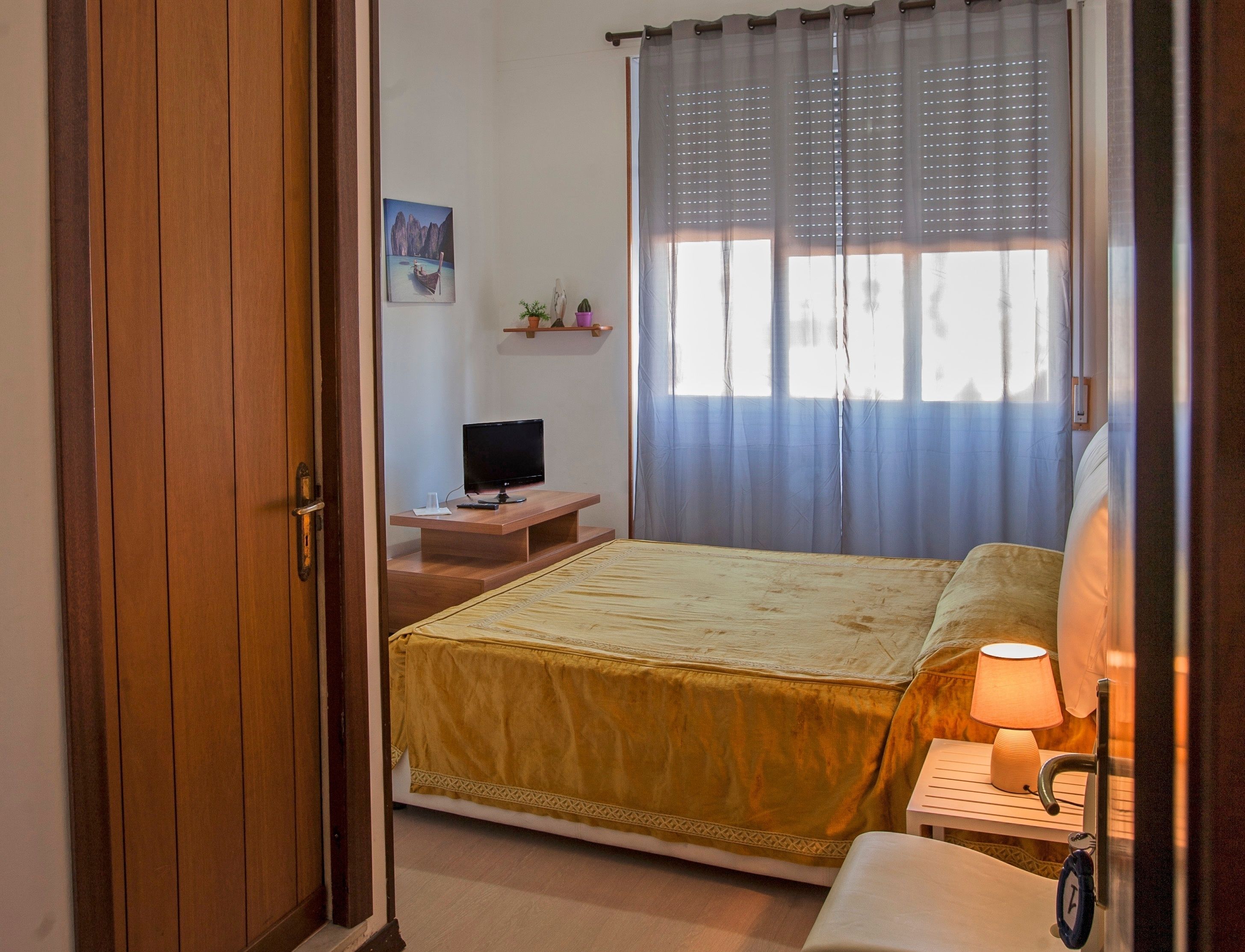 A bedroom with a bed, bedside table, lamp, and a television on a stand.