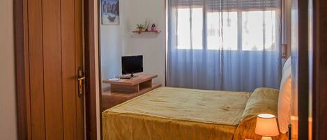 A bedroom with a bed, bedside table, lamp, and a television on a stand.