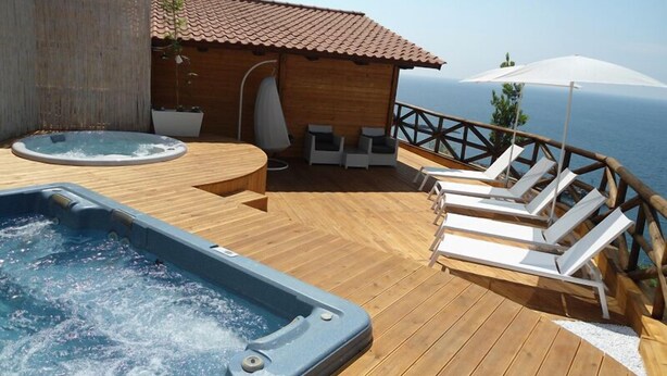 Eine Holzterrasse mit Whirlpool, Liegestühlen und Blick auf das Meer.