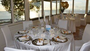 Ein Tisch ist für ein festliches Abendessen gedeckt, mit Kerzen, Gläsern und Blick auf das Meer.