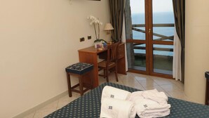 Ein Hotelzimmer mit einem Bett, einem Schreibtisch, einem Stuhl, einem Fernseher und Meerblick durch ein großes Fenster.