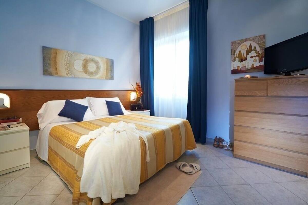 A hotel room with a large bed, a TV, a wooden dresser, and a painting on the wall.