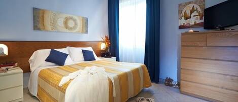 A hotel room with a large bed, a TV, a wooden dresser, and a painting on the wall.