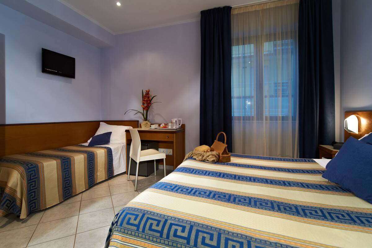 A hotel room with two beds, a desk, a chair, a TV, and a window with curtains.