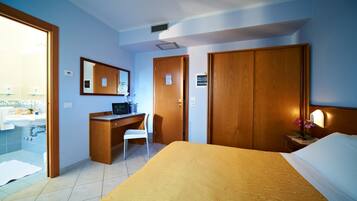 A hotel room with a bed, a desk, a chair, a bathroom with a sink, and a mirror.