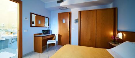 Een hotelkamer met een bed, een bureau, een stoel, een badkamer met een wastafel en een spiegel.