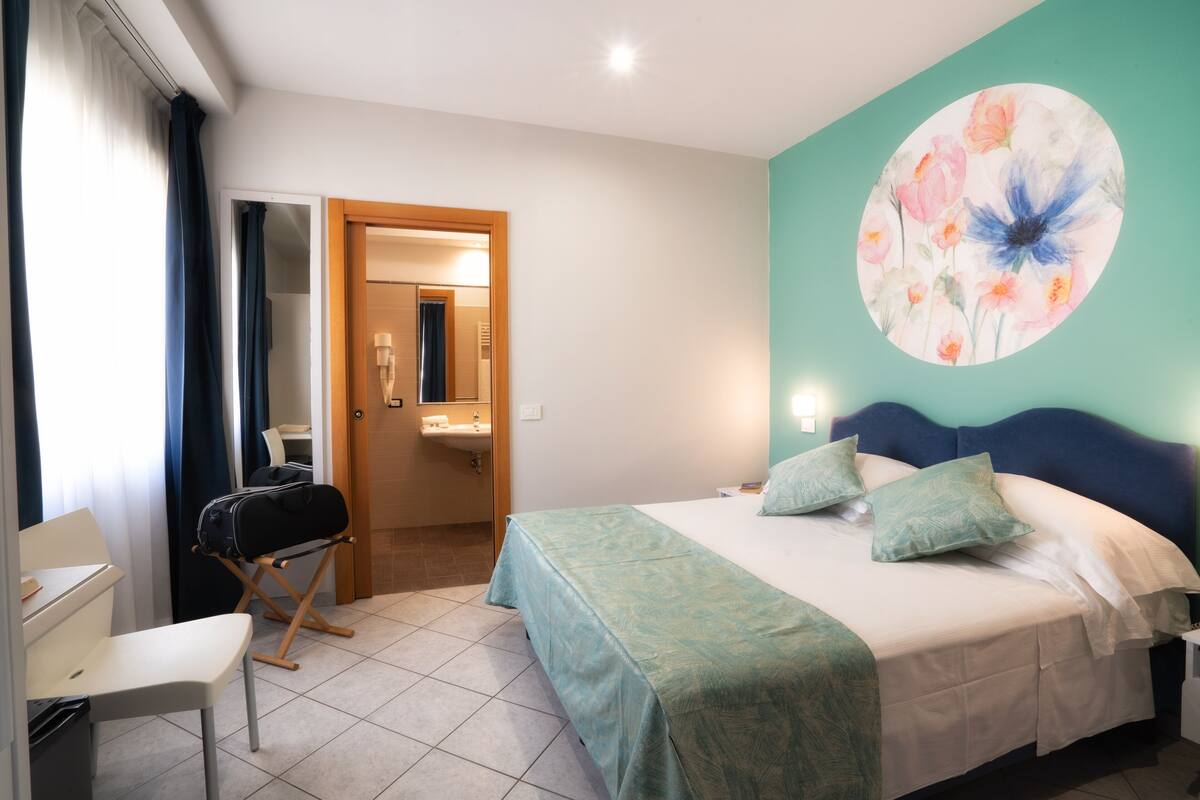 A hotel room with a bed, a desk, and a bathroom visible through an open door.