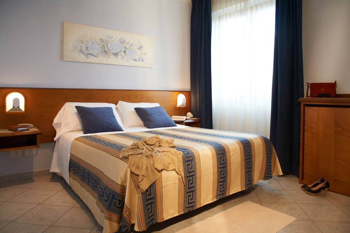 A neatly made bed with a patterned bedspread, a bedside table with a lamp, and a nightstand with a phone.