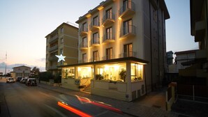 A multi-story hotel with balconies, a ground-level restaurant, and a visible star rating sign. - Hotel Sirio (Camaiore)