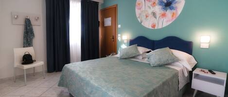 A bedroom with a bed, a nightstand, a chair, a door, and a wall with a floral painting.