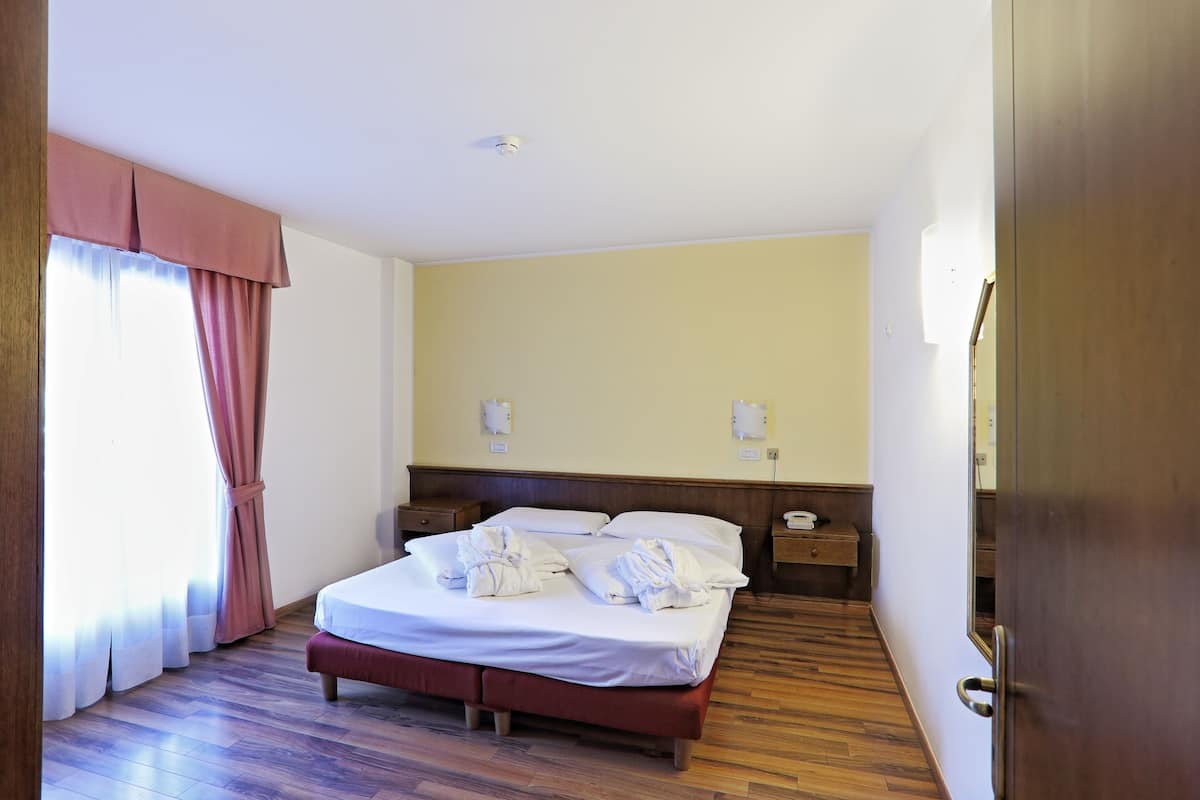 Ein Hotelzimmer mit Holzboden, einem Bett mit weißer Bettwäsche, einem Nachttisch und einem an der Wand befestigten Telefon.