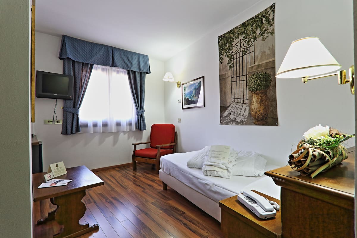 Ein Hotelzimmer mit Bett, Schreibtisch mit Telefon, Stuhl, Fernseher und einem Fenster mit Vorhängen.