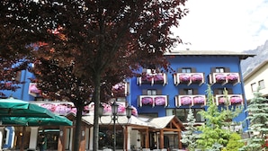 A building with balconies adorned with flowers, outdoor seating, and a tree in the foreground. - Hotel Baita Clementi (Bormio)