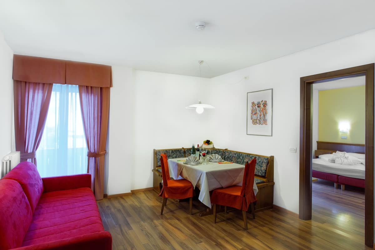 Ein Zimmer mit einem roten Sofa, einem Esstisch mit Stühlen, einer kleinen Bank und einem Bett.