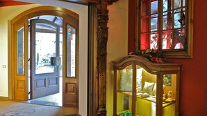 A hallway with a wooden door leading outside, a glass display cabinet with decorative items, and a red-framed window. - Hotel Baita Clementi (Bormio)