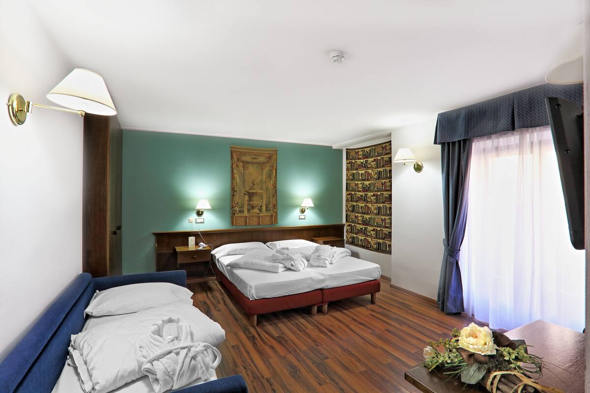 Ein Hotelzimmer mit zwei Betten, einem Bücherregal und einer dekorativen Blumenkomposition.
