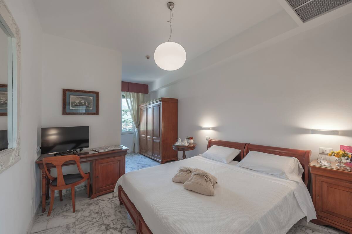 A hotel room with a bed, a desk with a chair, a television, and a wardrobe.