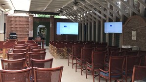 A covered outdoor seating area with rows of wicker chairs and tables, a brick wall, and a green ceiling. - Hotel President (Forte dei Marmi)