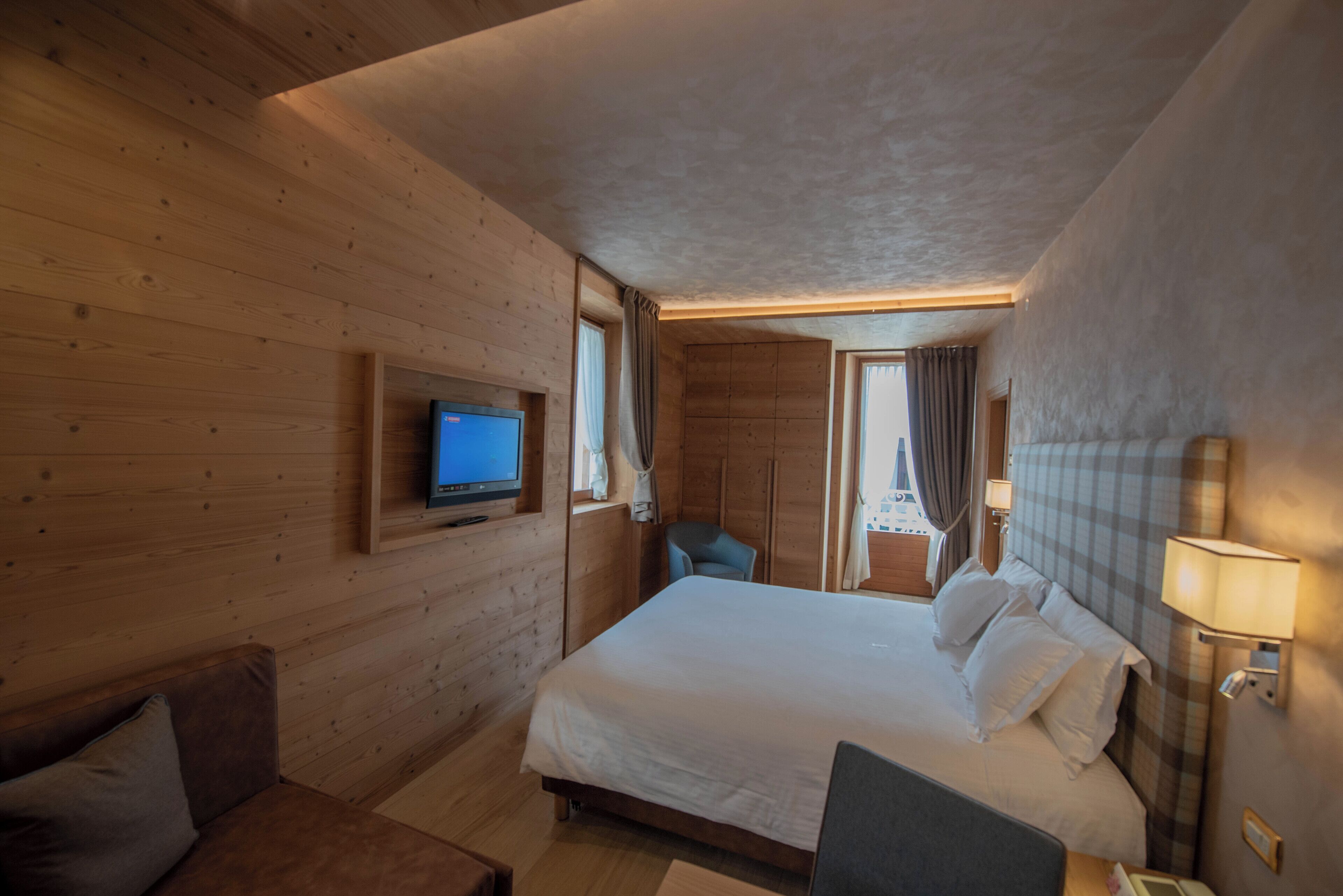 A wooden-paneled room with a large bed, a television, a desk, and a chair.