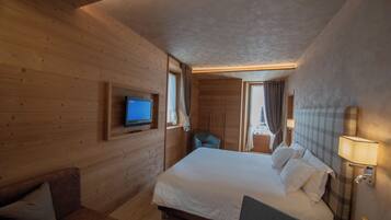 A wooden-paneled room with a large bed, a television, a desk, and a chair.