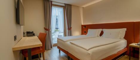 Habitación de hotel con cama, escritorio, silla, televisor y vista al exterior.