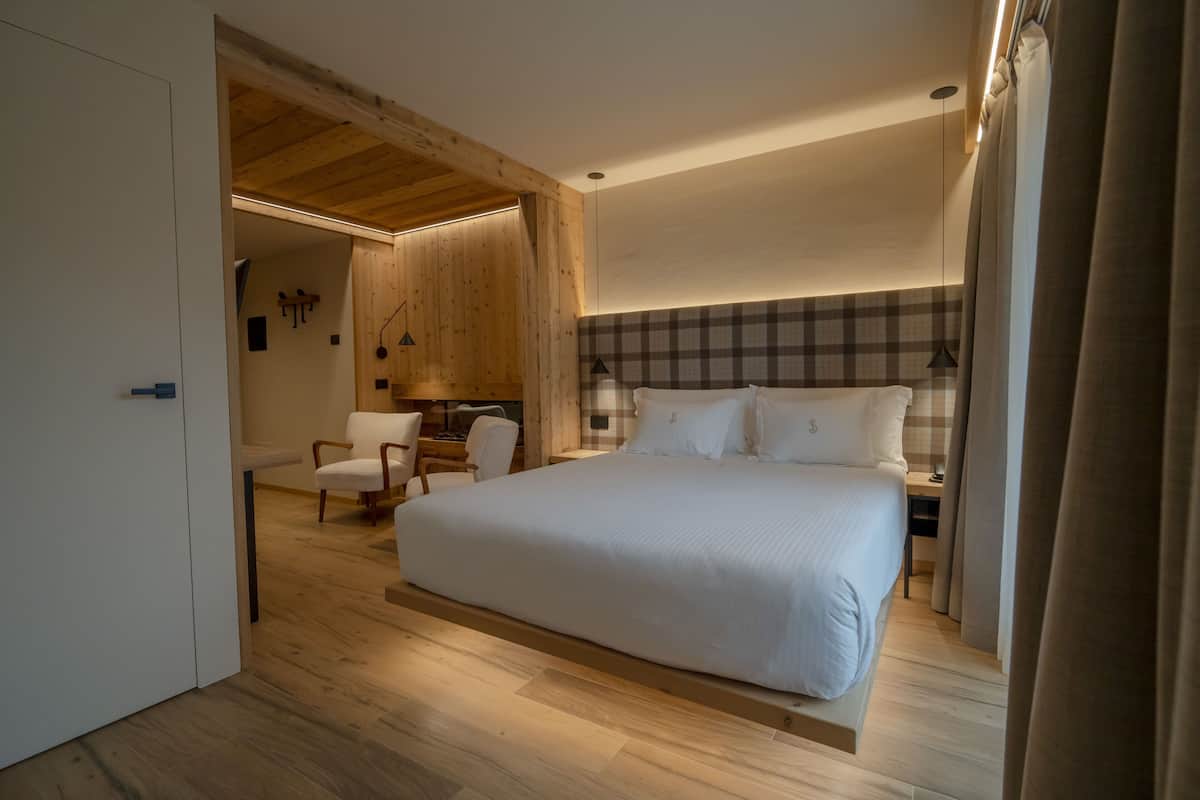 A bedroom with a large bed, wooden flooring, a checkered headboard, and a desk with a chair.