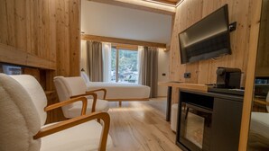 A cozy room with wooden walls, a flat-screen TV, a sofa, a chair, and a small kitchenette with a coffee machine. - San Lorenzo (Bormio)