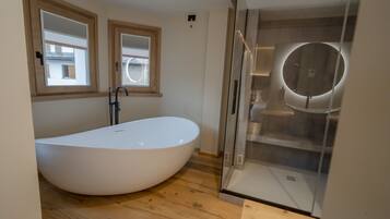 Une salle de bain moderne avec une baignoire sur pieds, une douche à parois de verre et deux fenêtres à cadre en bois.