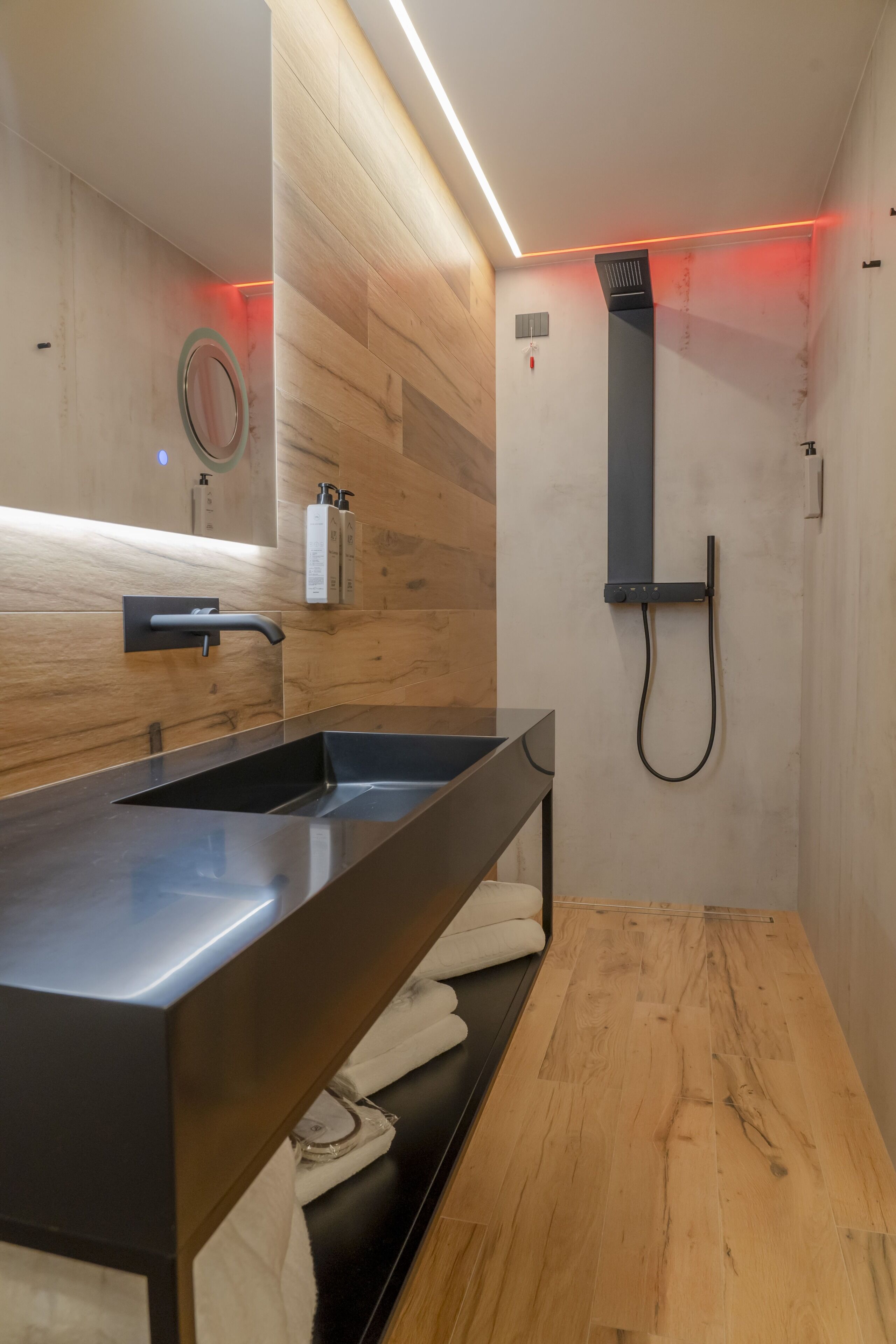 A modern bathroom with a wooden vanity, a large mirror, and a shower area.