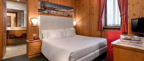 Une chambre à coucher aux murs lambrissés, avec un grand lit, une table de chevet, un miroir et un tableau représentant un paysage de montagne.