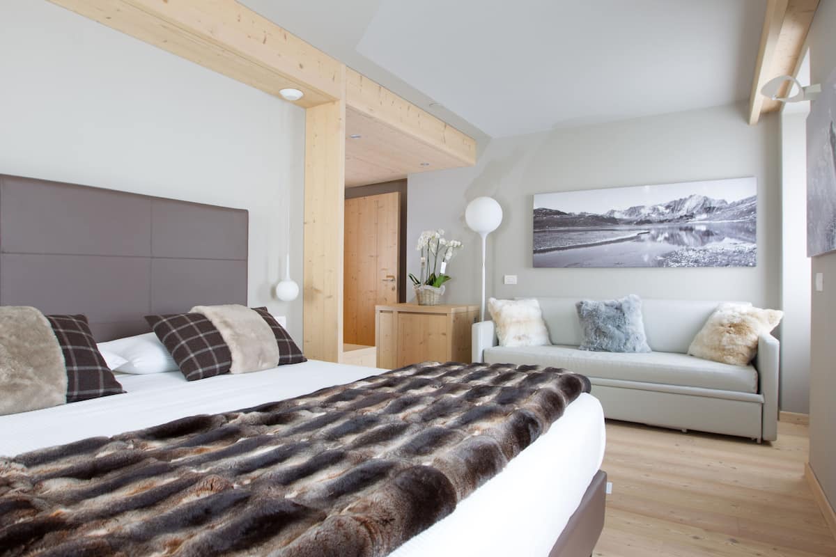 A modern bedroom with a large bed, a sofa, and a wall-mounted lamp.