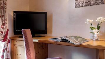 Ein Zimmer mit Schreibtisch aus Holz, Fernseher, Stuhl, Buch und einer Vase mit Blumen.